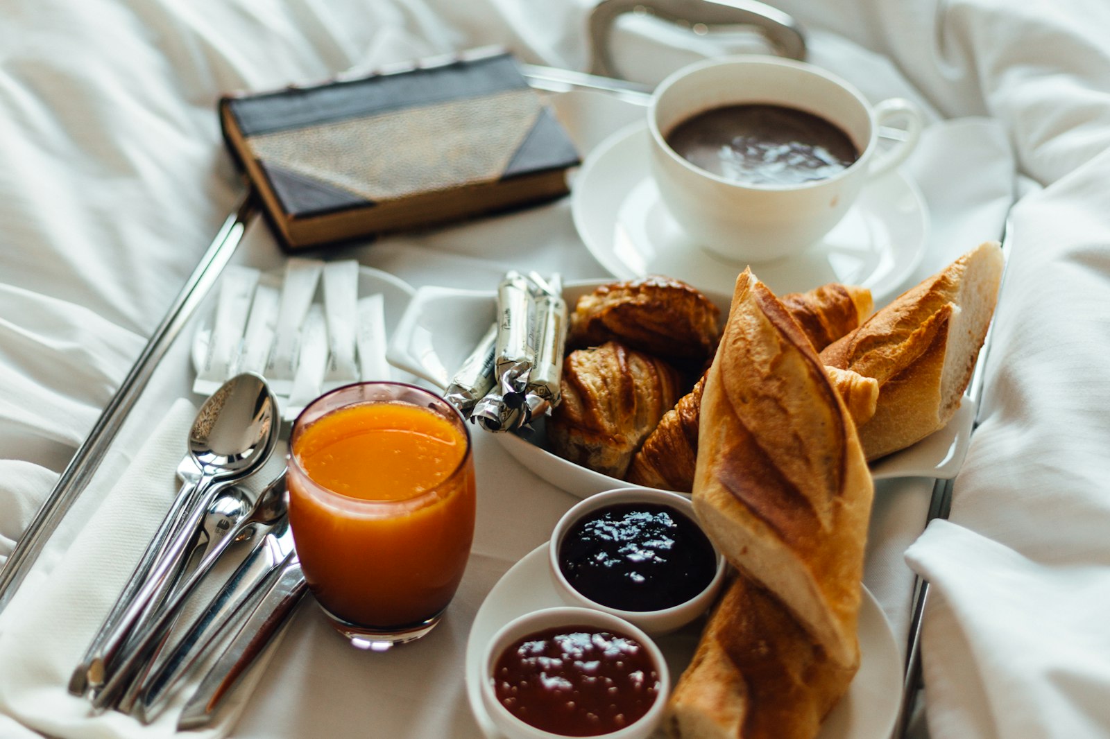 Room-service breakfast tray on white linen with coffee, juice, pastries and preserves