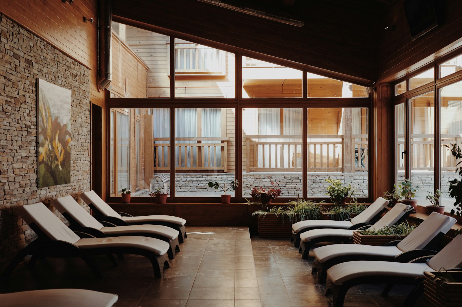 Sunlit spa relaxation room with wooden loungers, tall windows and potted greenery