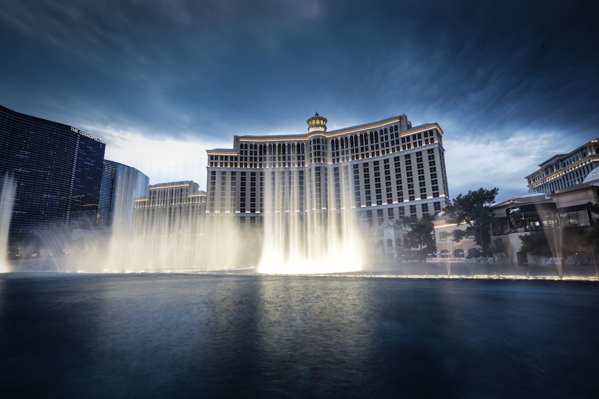 The Bellagio fountain show at dusk, seen from the public lakeside promenade